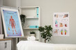 © Pixel-Shot - Interior of massage therapists office with couch, shelving unit and poster on flipchart in modern medical centre