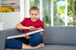 © Volodymyr - Child relaxing while reading a book at home. Happy kid exploring literature in home interior. Little reader enjoying bedtime story at home. Kid reading and learning in playroom.