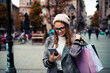 © Davor - Smiling woman with shopping bags using smartphone on city street