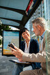 © Davor - Two business colleagues using smartphone at urban bus stop