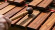 © naevermillion - Close up of a hand playing a wooden xylophone with a mallet.