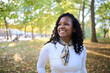 © CarlosBarquero - Smiling Black Latina millennial woman enjoying a sunny autumn park. Natural outdoor portrait with curly hair and scarf, conveying confidence, calm and positive travel lifestyle.