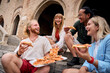 © CarlosBarquero - Group of cheerful young multi-ethnic friends enjoying pizza slices sitting on ancient stone steps during their summer vacation, having fun together