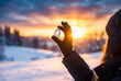 © Meow Creations - Hand wearing winter glove holding glowing clear crystal against vibrant sunset over snowy landscape