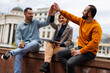 © Nikola Spasenoski - Friends enjoy time outdoors in a city sharing excitement during a casual meetup on a cloudy day near historic architecture with coffee cups in hand