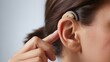 © MD - Close up view of a woman adjusting a discreet behind-the-ear hearing aid device for improved auditory clarity