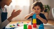 © Margarita Ratatosk - Woman teacher playing with child having Down syndrome at home. Caring tutor helping kid stack colorful plastic cups in room. Inclusive education and early childhood development concept.