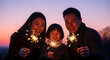 © rico - Happy Asian family holding glowing sparklers together at sunset in nature to celebrate a festive holiday moment with love and warmth