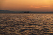 © Natalia - Cargo ship on a calm sea against a golden sunset with a mountainous coastline.