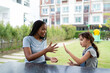 © Kawee - African female caregiver playing with Caucasian young girl outdoors in park.