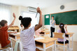 © Kawee - Group of diverse students raising hands to answer questions in classroom.