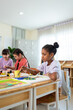 © Kawee - Diverse students coloring on painting board on table at elementary school.