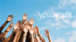 © PhotoArtHub - A group of diverse hands reach towards the sky with the word 'VOLUNTEER' formed by clouds, symbolizing unity and shared purpose
