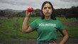 © Krakenimages.com - Woman volunteer in green shirt holding red heart aloft with raised hand, hand on hip and eyes closed in a forest; compassion charity solidarity.