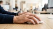 © tanin - Closeup of a man's hand using a computer mouse on a wooden desk in an office setting.