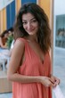 © Iryna - Young woman in coral sleeveless dress smiling at camera during indoor craft workshop for lifestyle portrait and background use