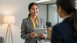 © Lubov - Professional Asian business woman wearing a grey suit and scarf holding a tablet. She is smiling and talking to a coworker in a bright modern office workspace