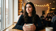 © sergign - Thoughtful young woman sitting at table holding coffee mug in cozy lighted cafe
