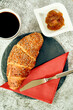 © Joachim - buttery croissant on ceramic plate with apricot jam and knife, set at cafe table. red napkin.