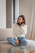 © gzorgz - Full length of a cheerful smiling confident woman sitting on the couch in her modern home