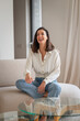 © gzorgz - Full length of a cheerful smiling confident woman sitting on the couch in her modern home