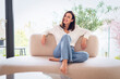 © gzorgz - Full length of a cheerful smiling confident woman sitting on the couch in front of a glass wall