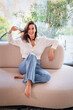 © gzorgz - Full length of a cheerful smiling confident woman sitting on the couch in front of a glass wall