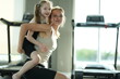 © ultramansk - Young woman and her girl in sportswear carry the girl on her back laughing in the gym after a family workout in the gym, shallow depth of field. Healthy active lifestyle of a modern family
