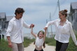 © ultramansk - Young parents and their playful child swing the child high while walking the sunny street on a walk through a new suburban housing development, shallow depth of field