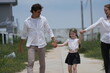 © ultramansk - Young couple with their laughing daughter swing the child high while walking the sunny street on a walk through a new suburban housing development, candid real moment