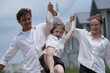 © ultramansk - Young parents and their playful child swing their laughing daughter by the arms as they walk on a walk through a new suburban housing development. Healthy active lifestyle of a modern family