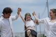 © ultramansk - Cheerful Caucasian family of three swing the child high while walking the sunny street among modern new houses of a suburban housing estate, authentic everyday scene