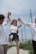 © ultramansk - Young parents and their playful child swing their laughing daughter by the arms as they walk on a walk through a new suburban housing development, candid real moment