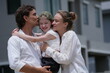 © ultramansk - Young couple with their laughing daughter kiss and hug their daughter while pointing at the new houses outdoors on the street of a newly built residential neighborhood
