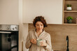 © La Famiglia - Woman enjoying morning coffee in pajamas at home kitchen
