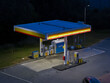 © AmazingAerialAgency - Krakow, Poland - 05 July 2026: Aerial view of a Shell station at night, featuring illuminated fuel pumps, a canopy with yellow and red branding, and a paved forecourt.