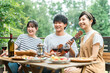 © buritora - Young Asian men and women, friends, colleagues, and coworkers enjoying a barbecue, home party, and glamping on a wooden deck.