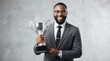 © Gophotograph - Successful African American businessman holding a silver trophy cup and smiling.
