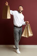 © Pixel-Shot - Happy young man with shopping bags near burgundy wall