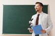 © Pixel-Shot - Male Science teacher with microscope and clipboard near blackboard in classroom