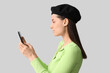© Pixel-Shot - Beautiful young woman in stylish black beret hat with mobile phone on grey background
