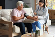 © Pixel-Shot - Young nurse measuring blood pressure of senior man at home