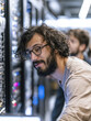© Siriroj - Man with curly hair and glasses inspects server racks