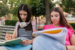 © PintoArt - Young female students studying together outdoors on park bench