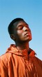 © Desingora - Portrait of a young black man with eyes closed wearing an orange jacket against a clear blue sky