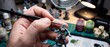 © Tanvir - Artist hand painting intricate details on miniature fantasy elf figurine using fine brush under magnifying lamp in creative studio