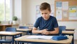 © Dzianis - young schoolboy sitting at a classroom desk holding his stomach in pain while looking down at an open notebook, showing abdominal cramps and discomfort during a school lesson