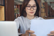 © tippapatt - Focused businesswoman reviewing business documents with laptop on table in modern office, workspace, business planning concept.