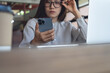 © tippapatt - Business woman thinking during using smartphone and working on laptop computer at cafe modern workspace, notebook on desk, online studying or remote work, corporate business concept, close up