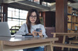 © tippapatt - Asian businesswoman using smartphone and working on laptop in cafe modern workspace, remote work, online business lifestyle. Student studying online, e-learning concept
